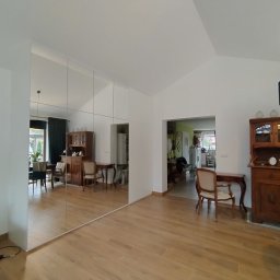 Piotr Białousz Woodshore - Lustrzana szafa wnękowa w salonie w Gdańsku, optycznie powiększająca przestrzeń. Widoczne odbicie mebli i detali wystroju wnętrza. Jasne, naturalne światło.