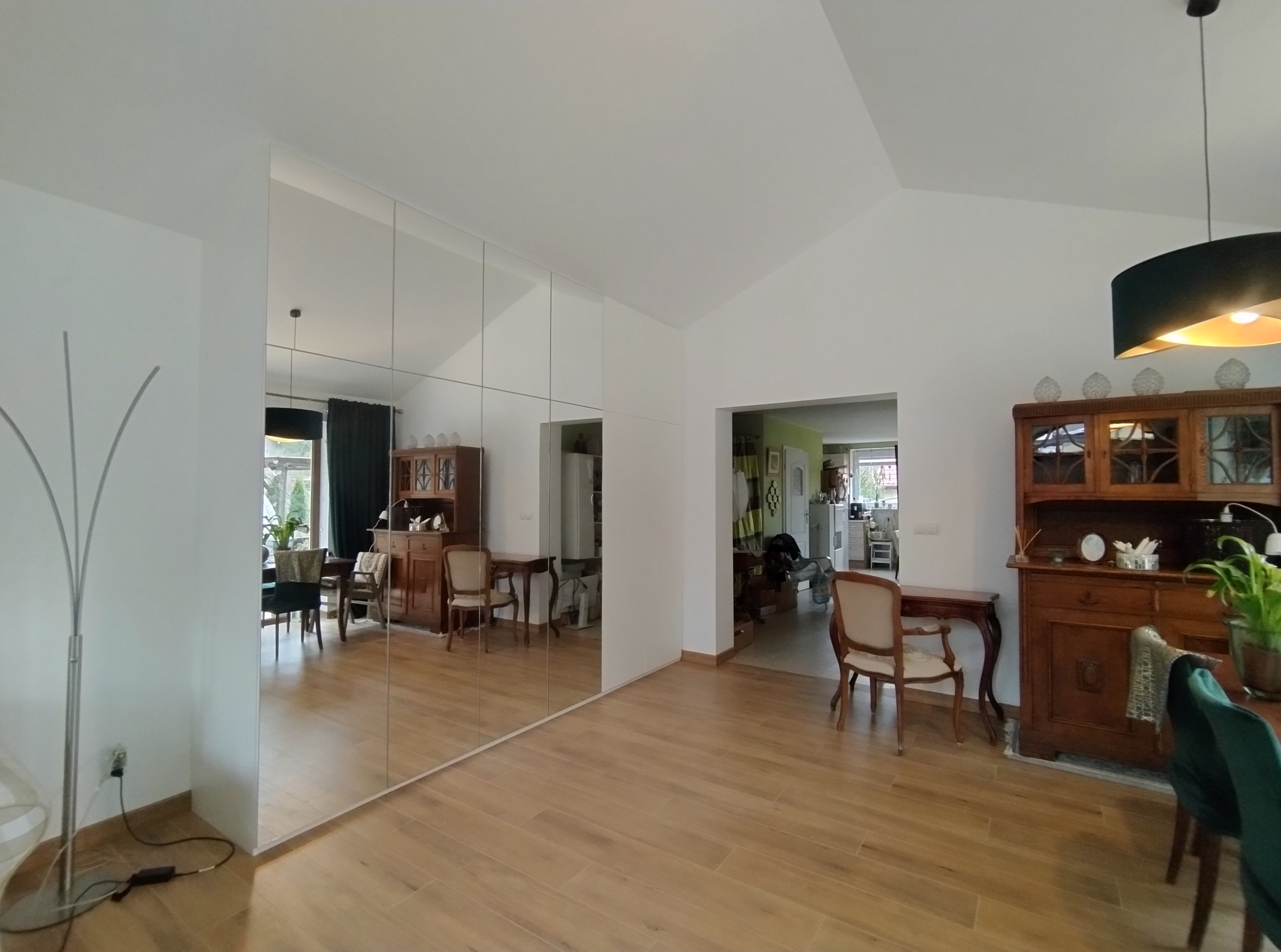 Lustrzana szafa wnękowa w salonie w Gdańsku, optycznie powiększająca przestrzeń. Widoczne odbicie mebli i detali wystroju wnętrza. Jasne, naturalne światło.