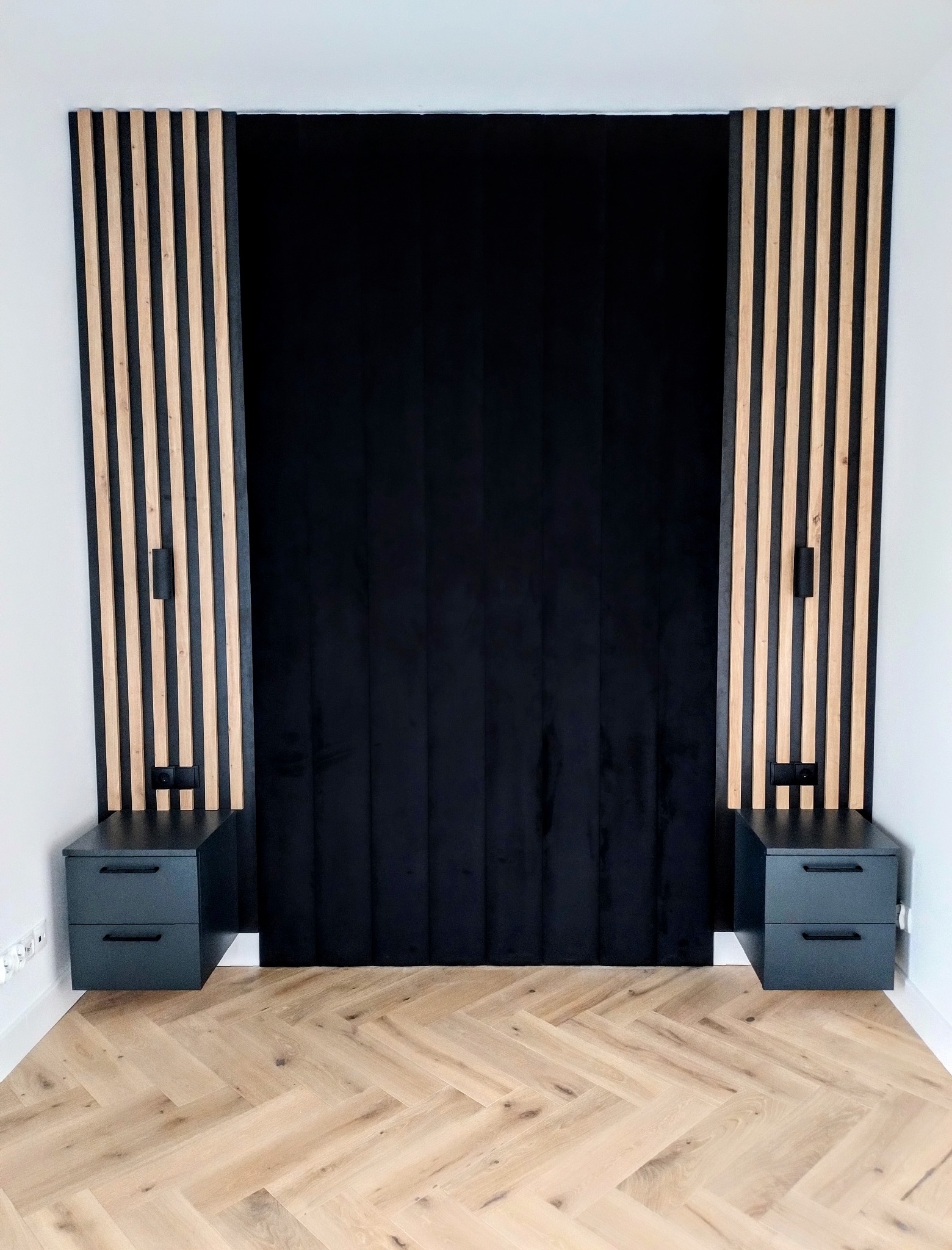 Panel tapicerowany za łóżkiem z drewnianymi lamelami po bokach i szafkami nocnymi. Parkiet ułożony w jodełkę. Minimalistyczny design sypialni.