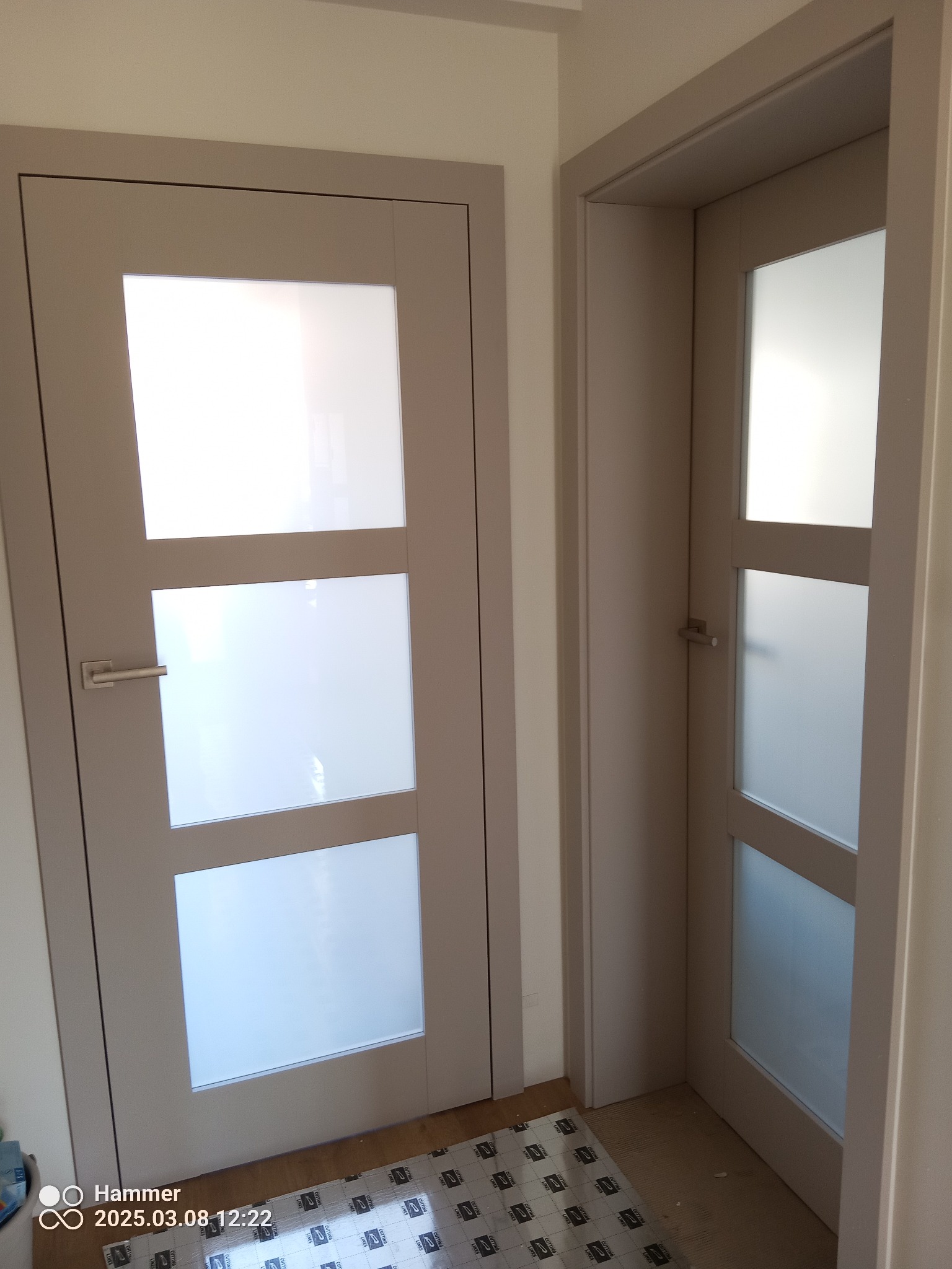 Dwa beżowe, przeszklone drzwi wewnętrzne z trzema panelami z matowego szkła, widoczne z bliska. Jeden zestaw drzwi jest otwarty, drugi zamknięty.