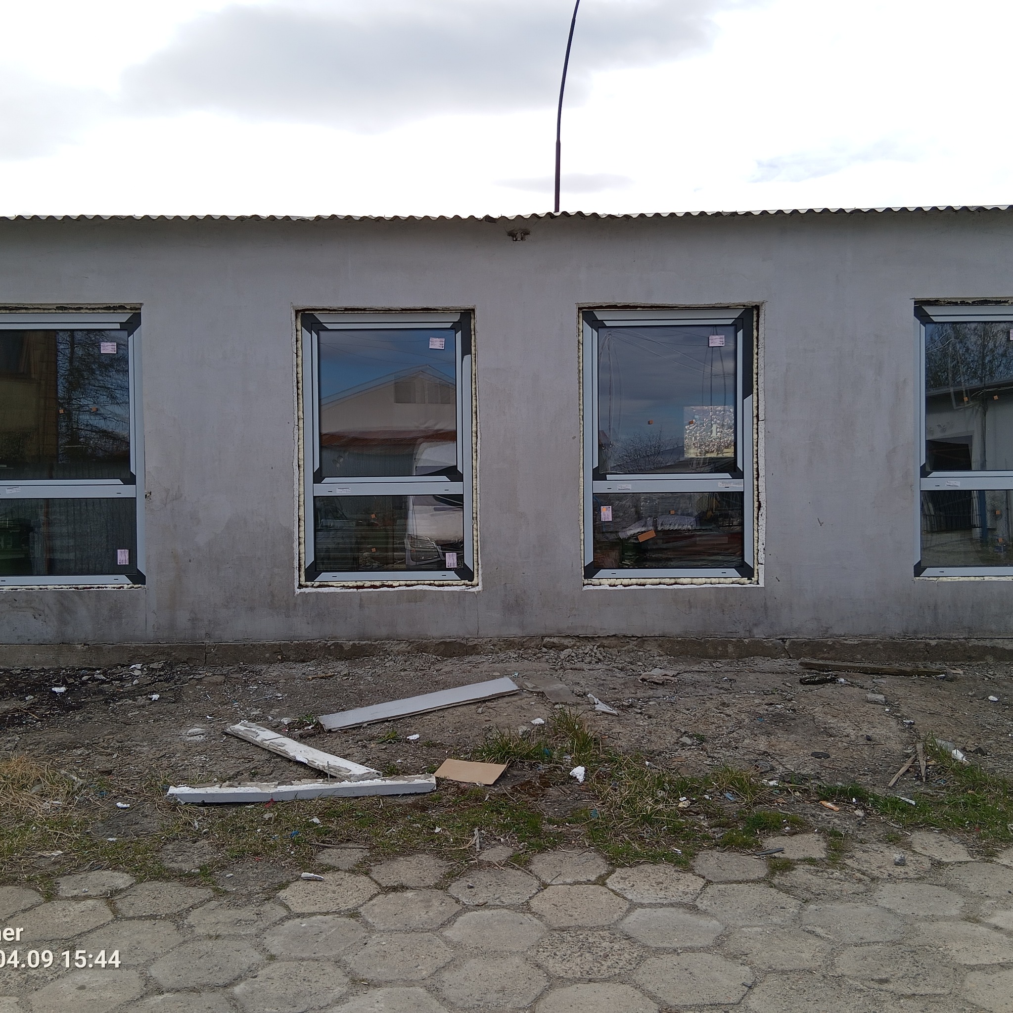 Szare okna PCV z pianką montażową w surowej elewacji budynku. Widoczne ślady prac budowlanych na zewnątrz. Ujęcie z dołu, pochmurne niebo w tle.