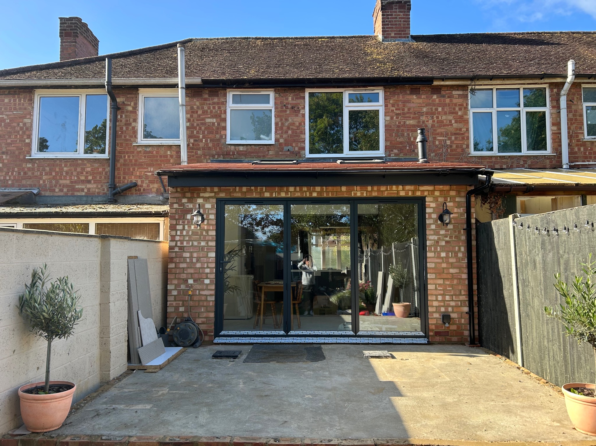 Nowoczesne, przesuwne drzwi tarasowe w ceglanym domu jednorodzinnym. Widoczne elementy wykończenia i przygotowany taras. Jasne, słoneczne światło.