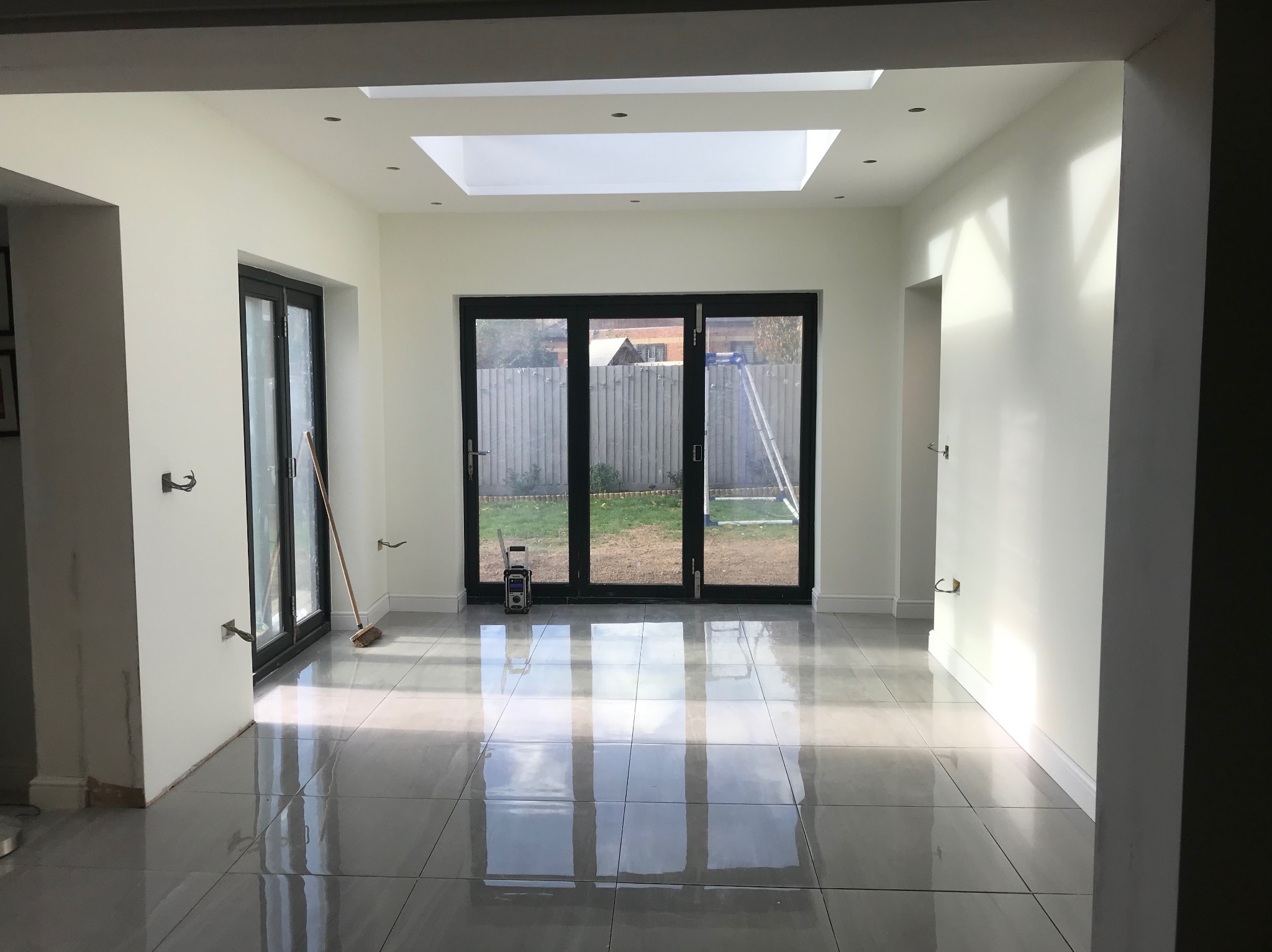 Jasne wnętrze po remoncie: szare płytki podłogowe odbijają światło z okien dachowych i drzwi balkonowych. Ściany białe, gładkie, z widocznymi elementami instalacji.