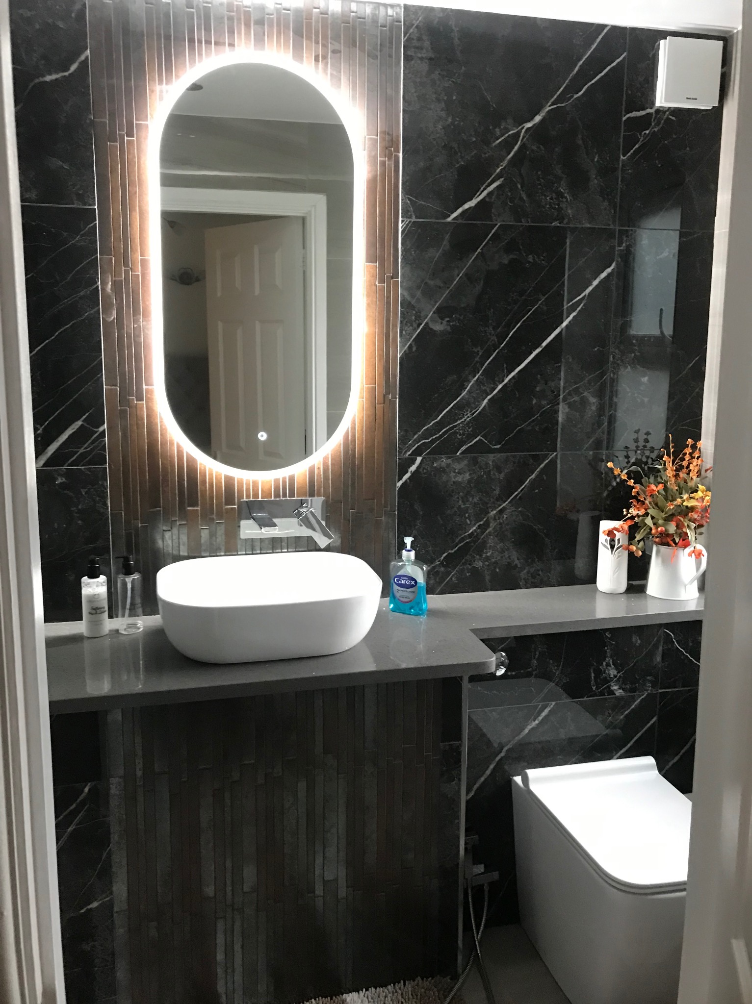 Nowoczesna łazienka w Białymstoku z umywalką nablatową, podświetlanym lustrem i czarnymi płytkami imitującymi marmur. Eleganckie wykończenie.