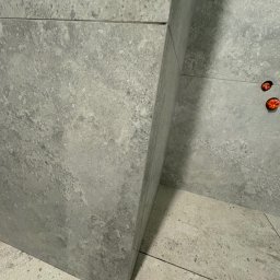 VEBud-pro - Szara, matowa ściana i podłoga wyłożona płytkami imitującymi beton. Widoczne gniazdka elektryczne. Minimalistyczne wykończenie wnętrza, surowy styl.