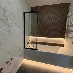 VEBud-pro - Nowoczesna łazienka z wanną i kabiną prysznicową w czarnej ramie. Marmurowe płytki, drewniane panele ścienne i podświetlenie LED tworzą elegancki klimat.