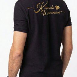 K.B. sp. z o.o. - Czarna koszulka polo z nadrukiem w kolorze złotym 'Kapsuła Wspomnień' z motywem diamentu, widok z tyłu na białym tle. Precyzyjny nadruk na odzieży.