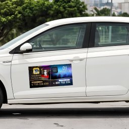 K.B. sp. z o.o. - Biały samochód z naklejkami reklamowymi na drzwiach, prezentującymi usługi DJ i wypożyczalni maskotek. Widoczne numery telefonów kontaktowych i nazwy firm.