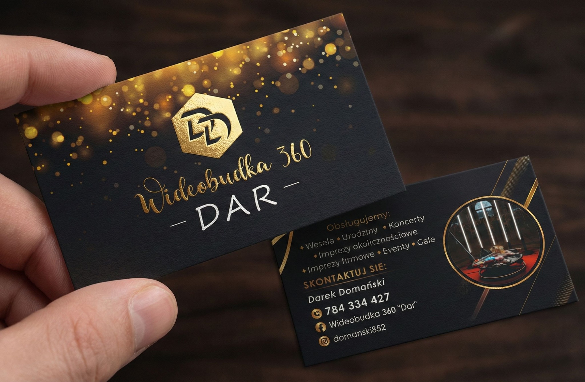Eleganckie wizytówki w odcieniach czerni i złota, z błyszczącym logo i detalami, prezentowane w dłoni na ciemnym, drewnianym tle. Widoczny kontakt do firmy.