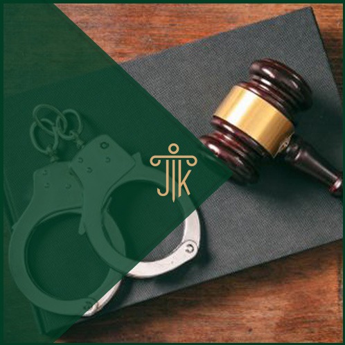 Młotek sędziowski, kajdanki i logo kancelarii na ciemnym tle. Symbol sprawiedliwości i prawa karnego w ujęciu z góry.