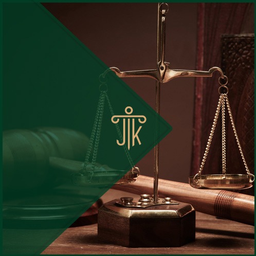 Złote wagi Temidy na drewnianym stole, z zielonym trójkątnym logo JJK w lewym górnym rogu. W tle książki i drewniany młotek sędziowski.