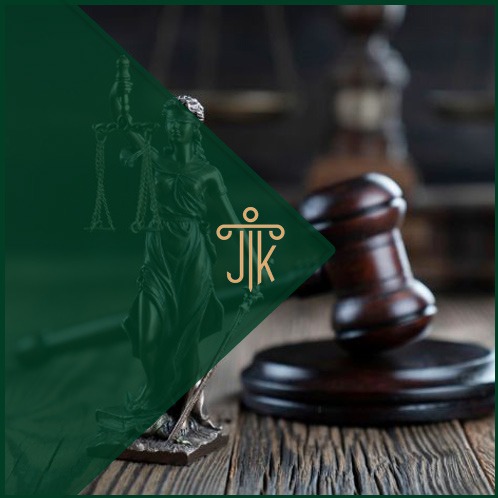 Temida z wagą i młotek sędziowski na drewnianym stole, z logo kancelarii w zielonym trójkącie. Symbol sprawiedliwości i prawa.