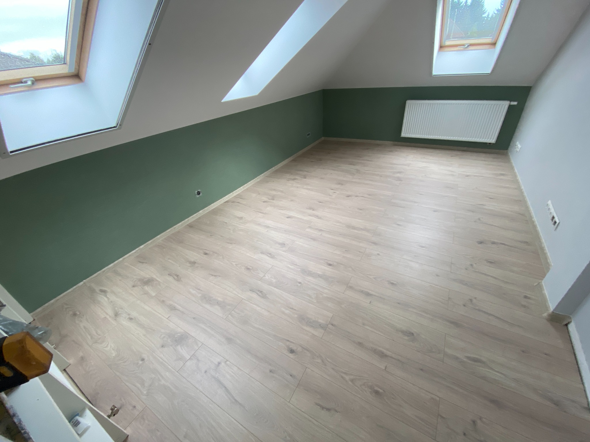 Poddasze po remoncie: świeżo pomalowane ściany w odcieniach zieleni i szarości, jasna podłoga z paneli, okna dachowe w skosach.