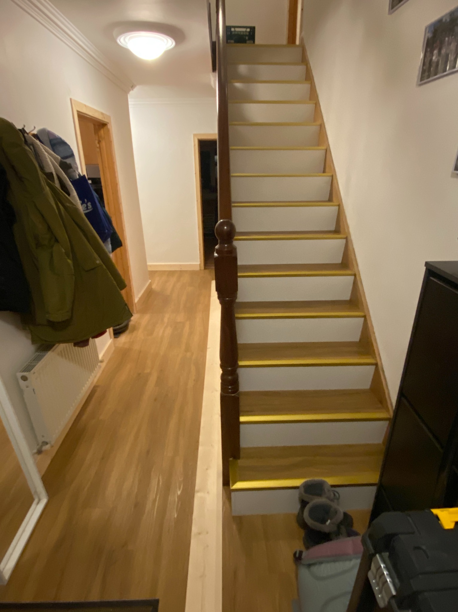 Montaż paneli winylowych na stopniach z białą podstopnicą i złotą listwą wykańczającą.