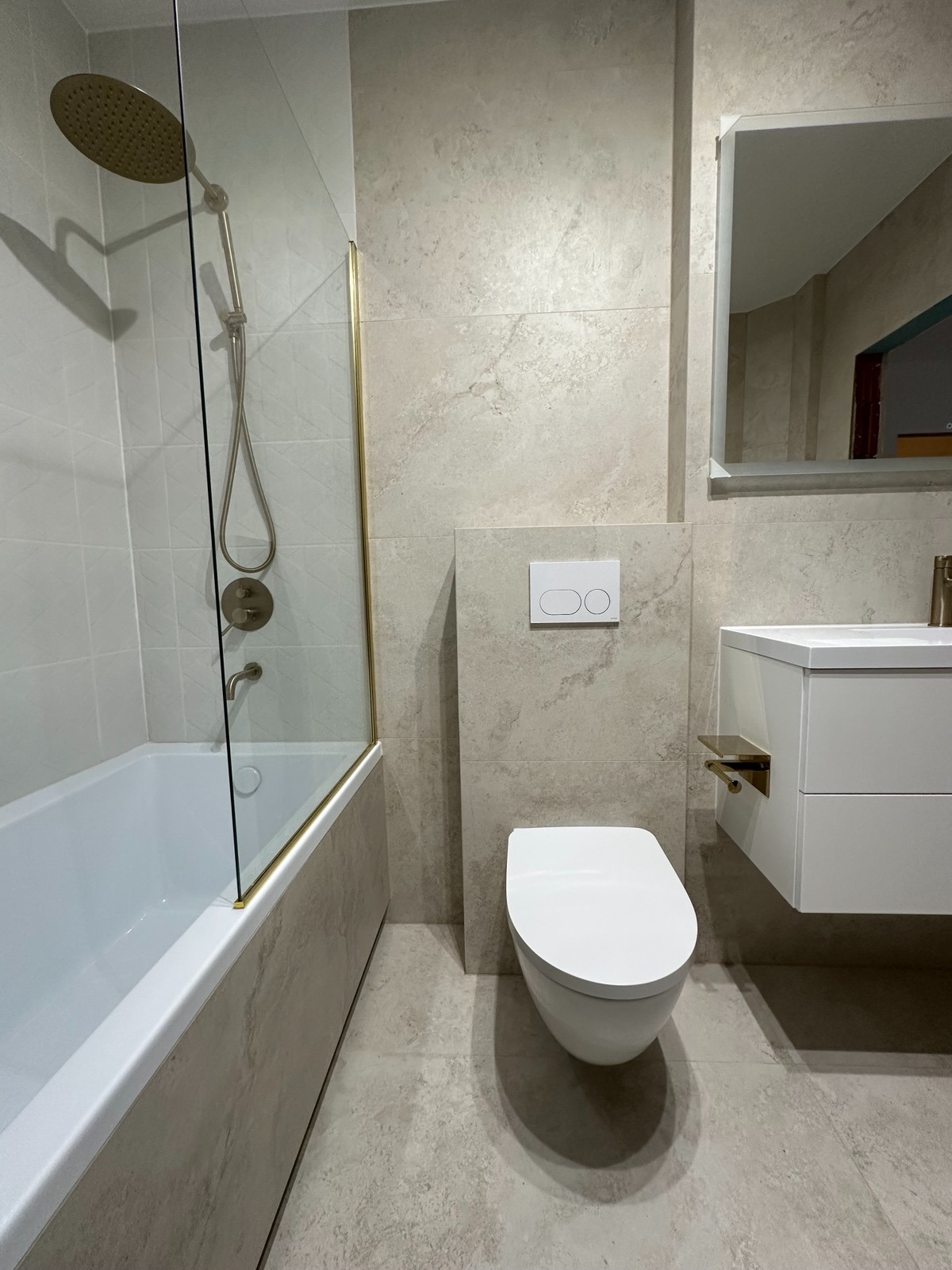 Wykończona łazienka w beżowych płytkach z kabiną prysznicową ze złotymi detalami, podwieszaną toaletą i umywalką. Nowoczesny design z dbałością o szczegóły.