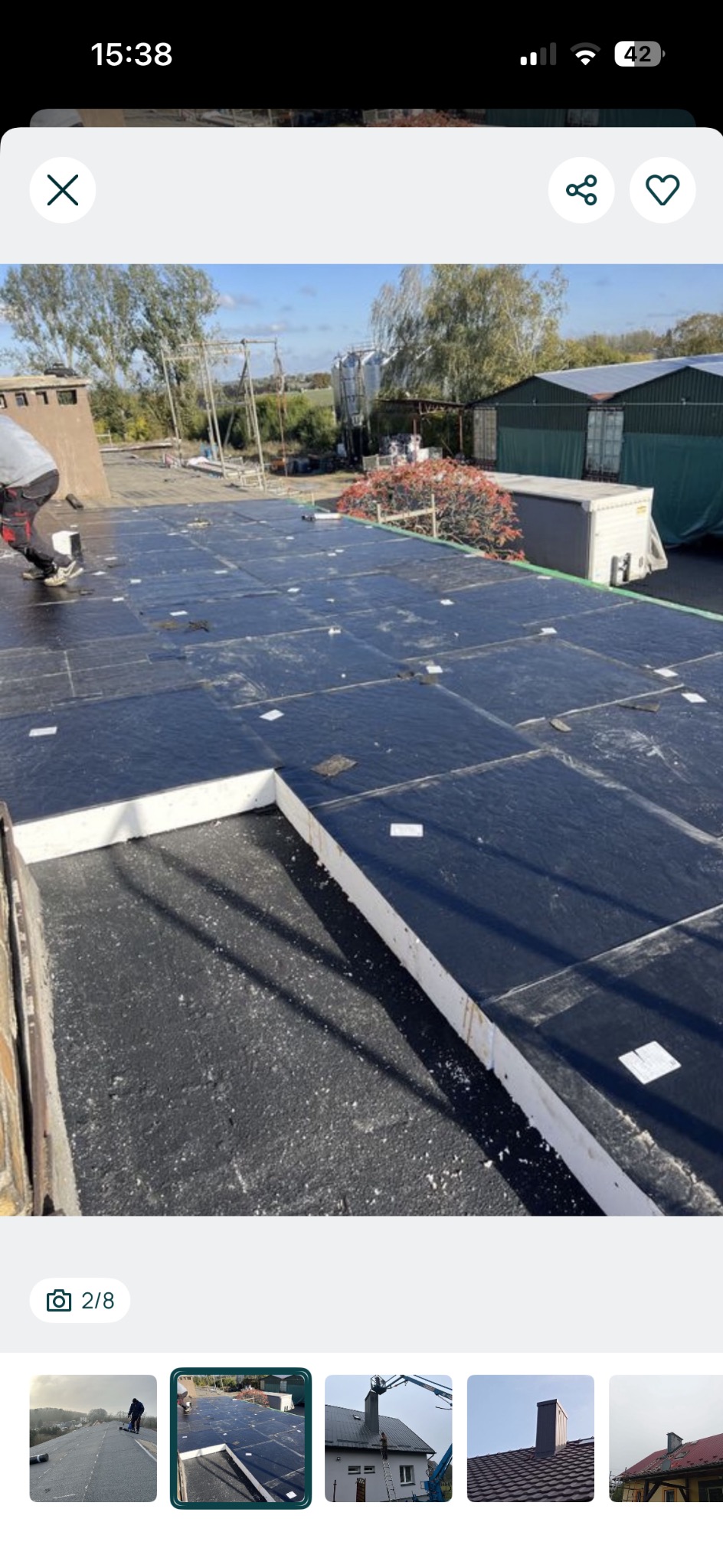 Czarny dach pokryty izolacją z białymi płytami styropianowymi, widok z góry. W tle budynki gospodarcze i drzewa. Prace dekarskie w toku.