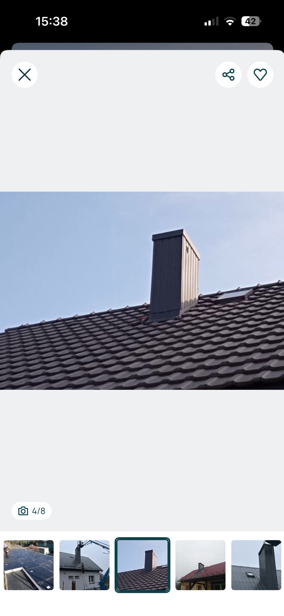 Ciemna dachówka ceramiczna na dachu domu z nowym, metalowym kominem na tle błękitnego nieba. Widok z dołu, podkreślający strukturę dachu.