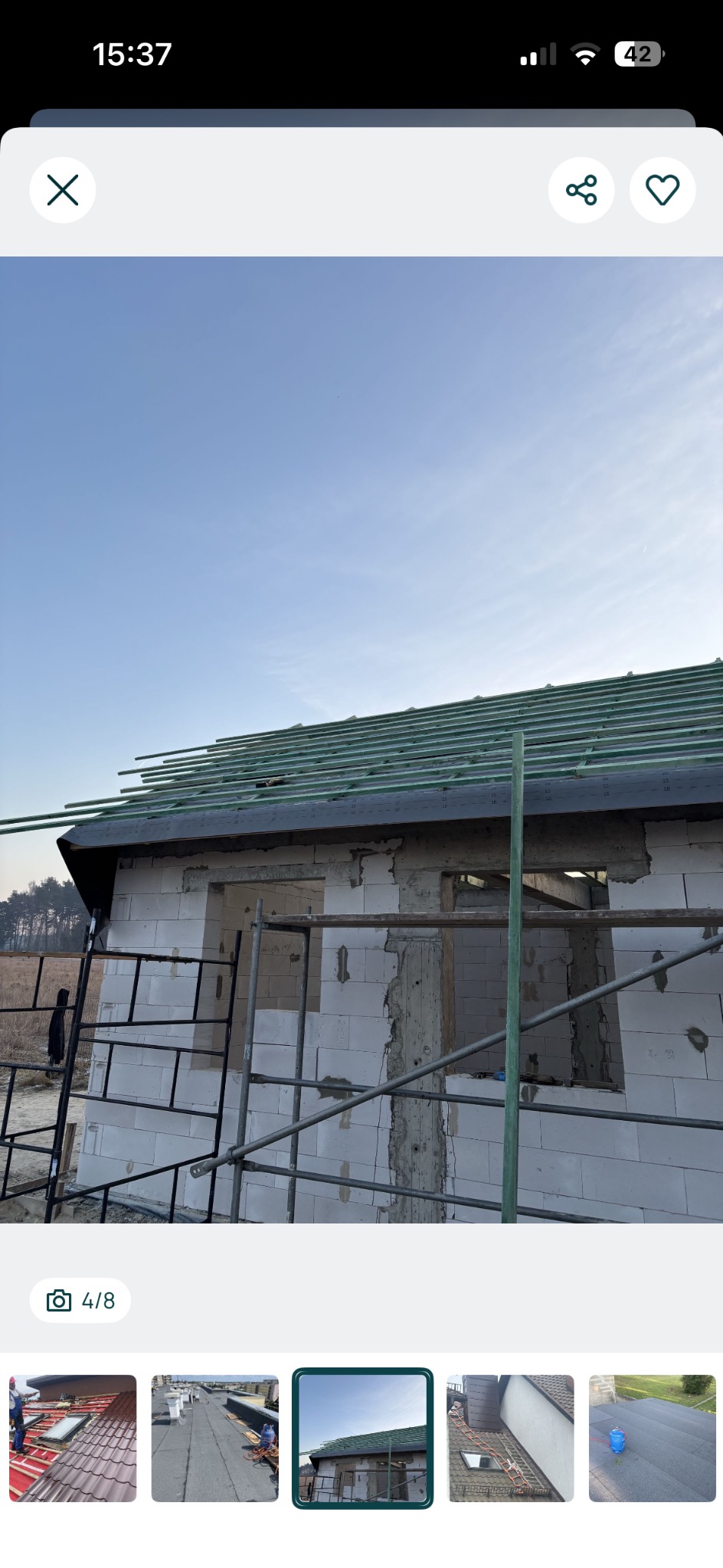 Budowa dachu domu jednorodzinnego w trakcie realizacji. Widoczne rusztowania i elementy konstrukcji dachu na tle błękitnego nieba. Ujęcie z dołu.