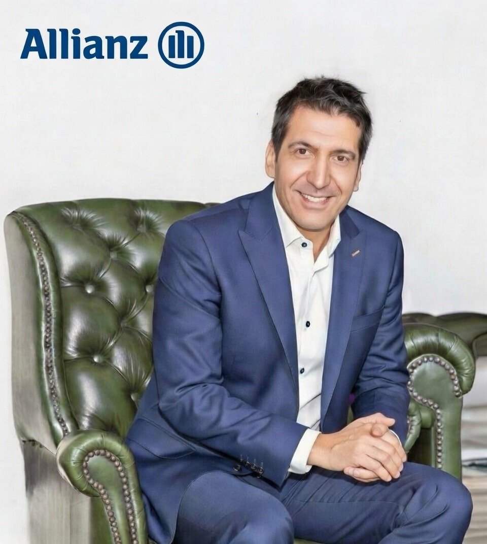 Uśmiechnięty mężczyzna w garniturze siedzi w skórzanym fotelu na tle logo Allianz. Profesjonalny wizerunek doradcy finansowego.