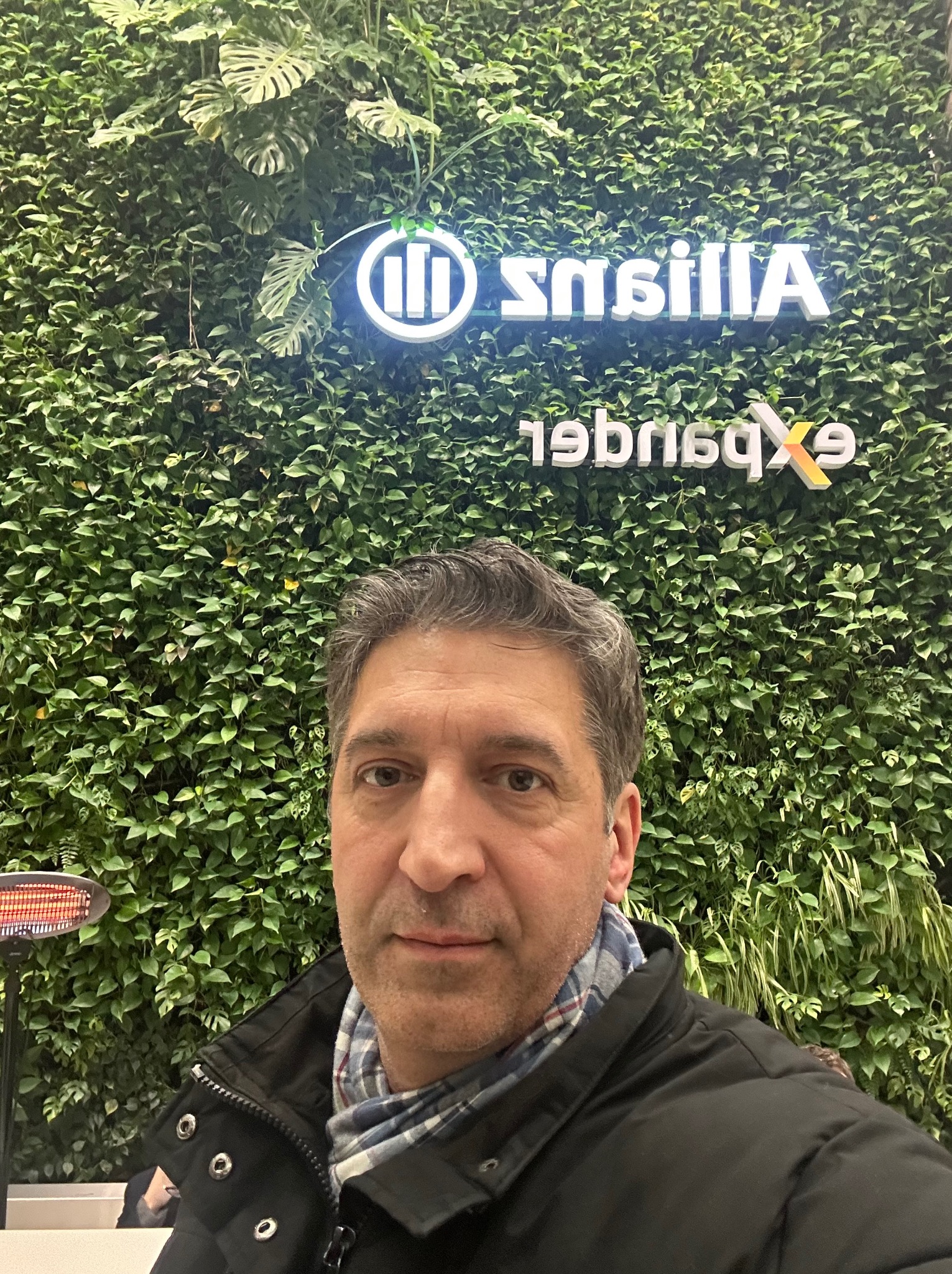 Mężczyzna na tle ściany z roślin z logo Allianz i Expander. Nietypowe ujęcie z bliska, z widocznym fragmentem grzejnika.