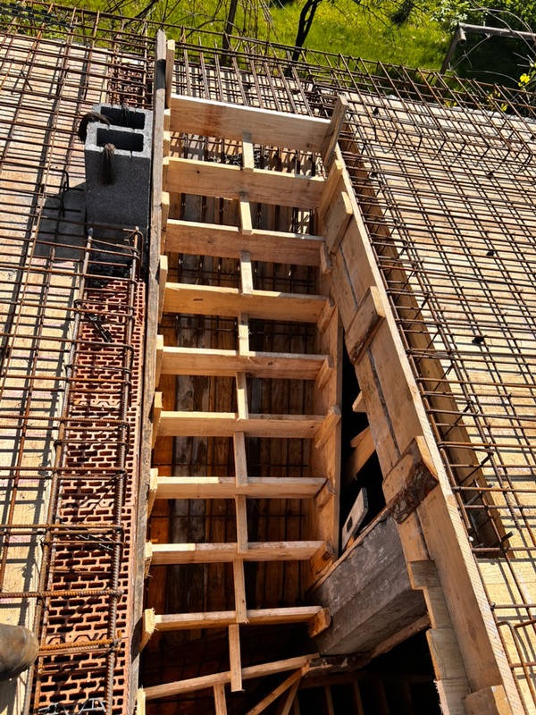 Zbrojenie stropu z drewnianym szalunkiem i pustakami wentylacyjnymi. Widok z góry na konstrukcję w trakcie budowy, z zielenią w tle.