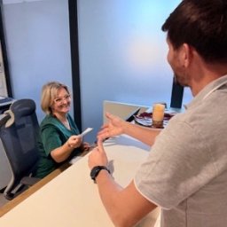 Beskid Clinic - Uśmiechnięta recepcjonistka w zielonym uniformie podaje dokument pacjentowi przy jasnej ladzie recepcyjnej w nowoczesnej klinice. Pacjent wskazuje palcem na dokument.