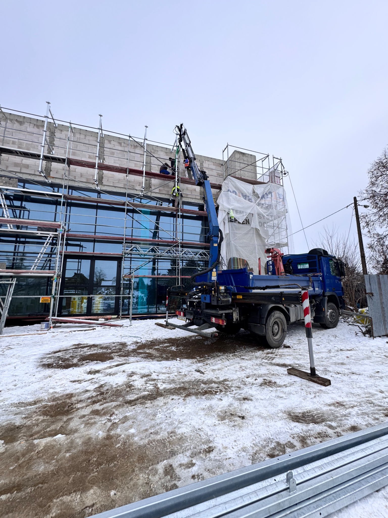 Montaż okien na rusztowaniu przy użyciu dźwigu samochodowego. Budynek w trakcie budowy, zimowa sceneria.