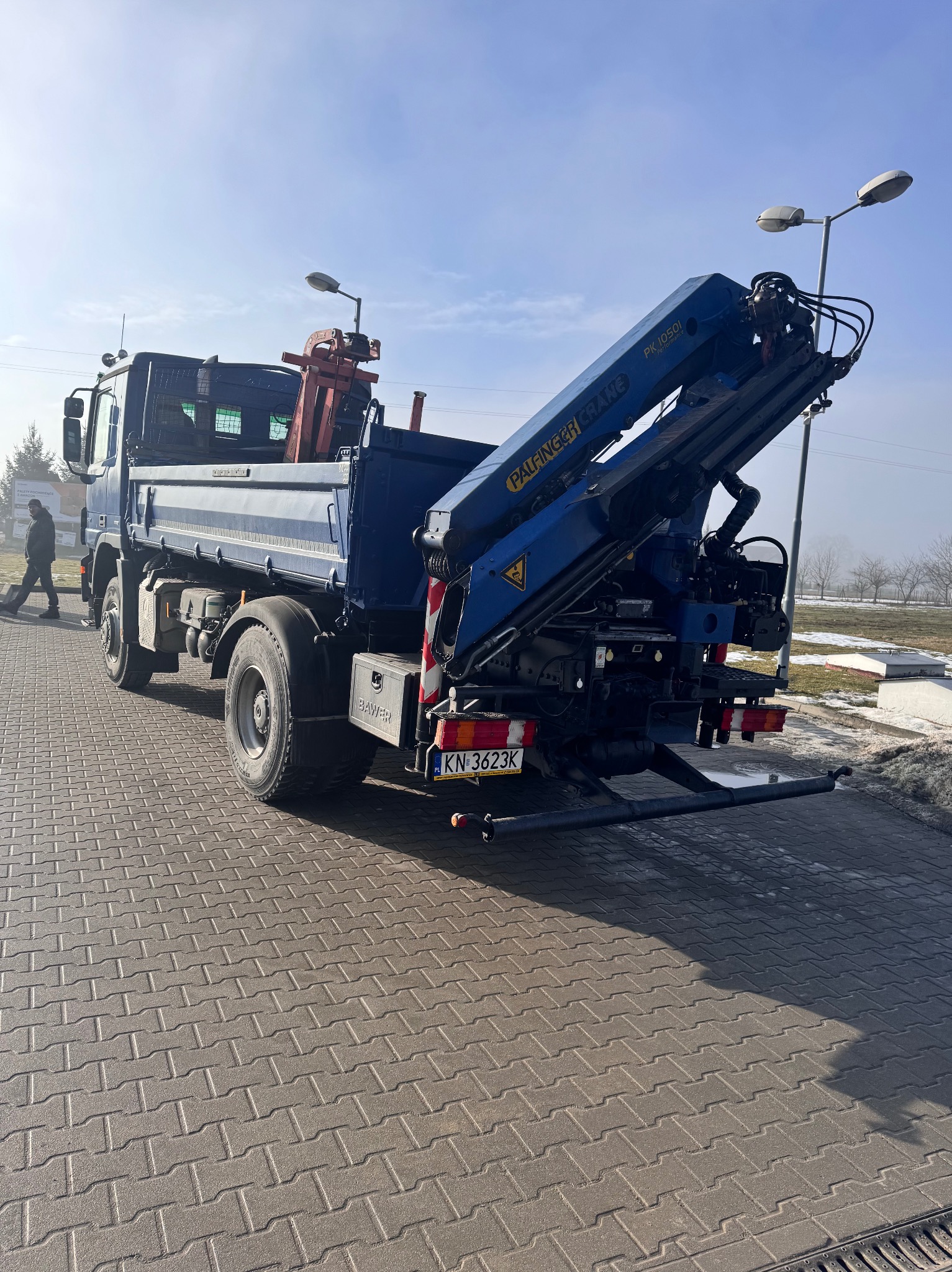 Ciężarówka z dźwigiem Palfinger Crane PK 10501 na kostce brukowej, widok z tyłu, tablica rejestracyjna KN 3623K, osoba w tle po lewej stronie.