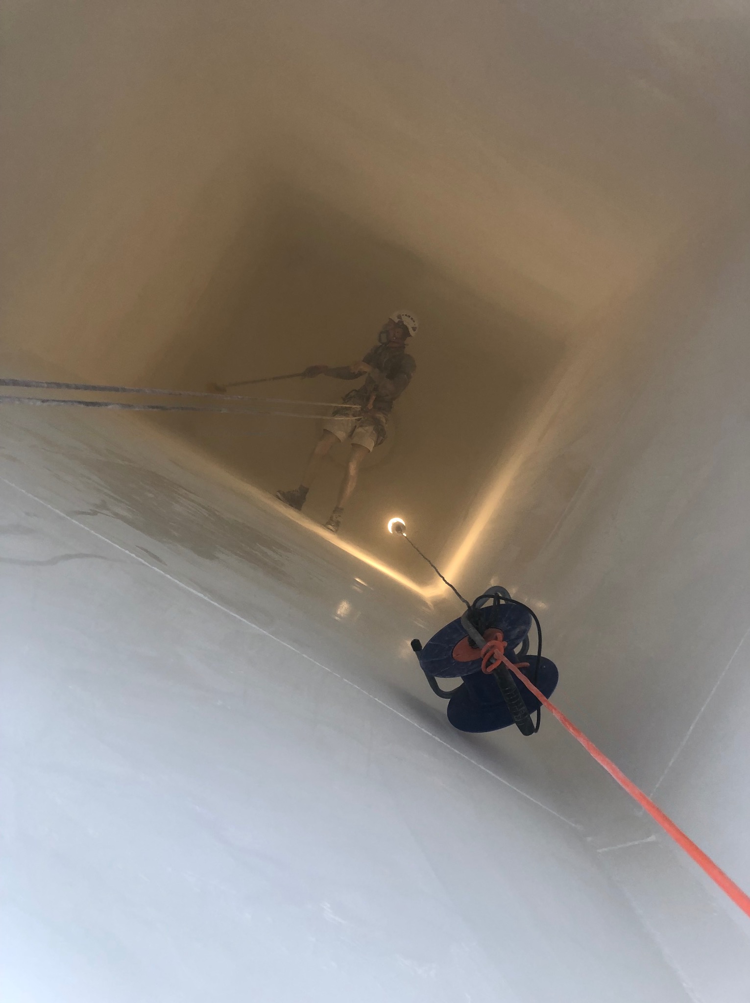 Pracownik na linie wewnątrz jasnej konstrukcji, prawdopodobnie komina, podczas inspekcji lub czyszczenia. Usługi wysokościowe w Piastowie.