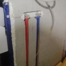 G&O - Instalacja wodna w łazience: czerwona i niebieska rura doprowadzona do zaworów, widoczne przewody elektryczne i stelaż podtynkowy. Surowy stan, przygotowanie do wykończenia.
