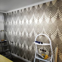 G&O - Ściana z tapetą w stylu art deco, widoczne drabiny malarskie i narzędzia. Dekoracyjne wykończenie wnętrza z wzorem wachlarzy.