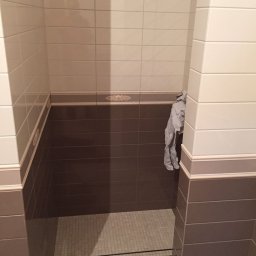 Wykończona kabina prysznicowa z brązowo-białymi płytkami, dekoracyjnym pasem i odpływem liniowym. Widok z góry, wnętrze łazienki po remoncie.