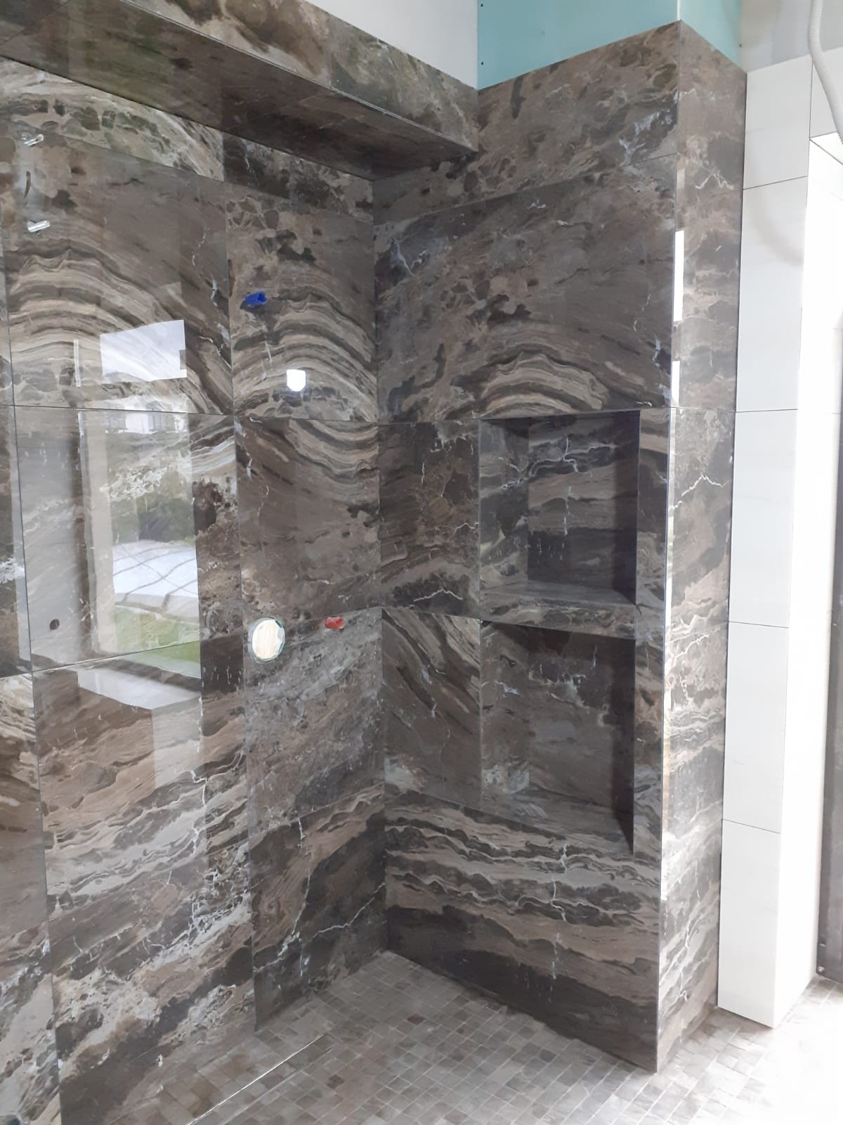 Wykończona kabina prysznicowa z półkami wnękowymi, wyłożona brązowymi płytkami imitującymi marmur. Realizacja z Poznania.