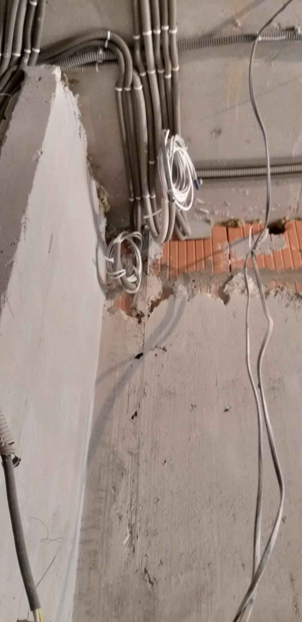 Instalacja elektryczna w peszlach na surowym suficie i ścianach z ceglanymi elementami. Widoczne kable i przewody w trakcie montażu.