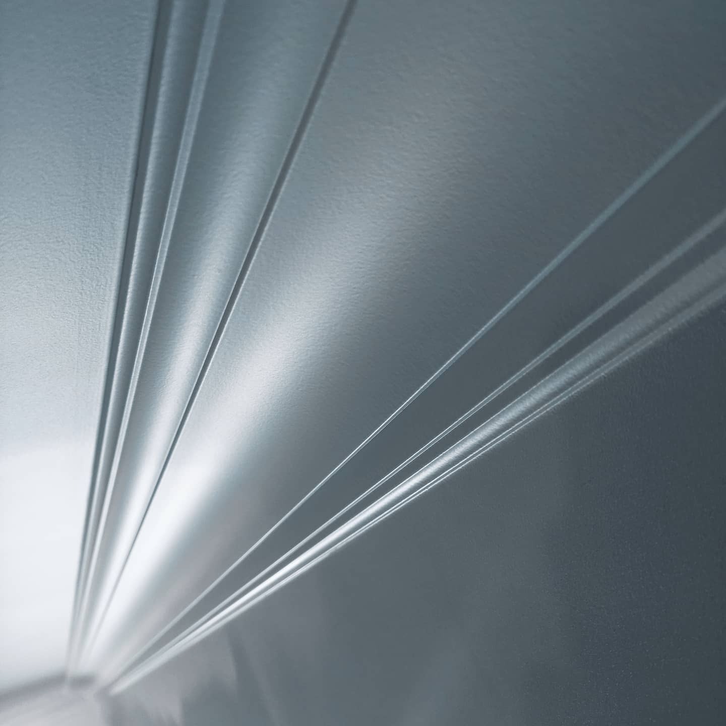 Szare panele ścienne z delikatnymi, wypukłymi liniami, ułożone pod kątem, tworzące nowoczesny wzór. Gładka powierzchnia z subtelnym połyskiem.