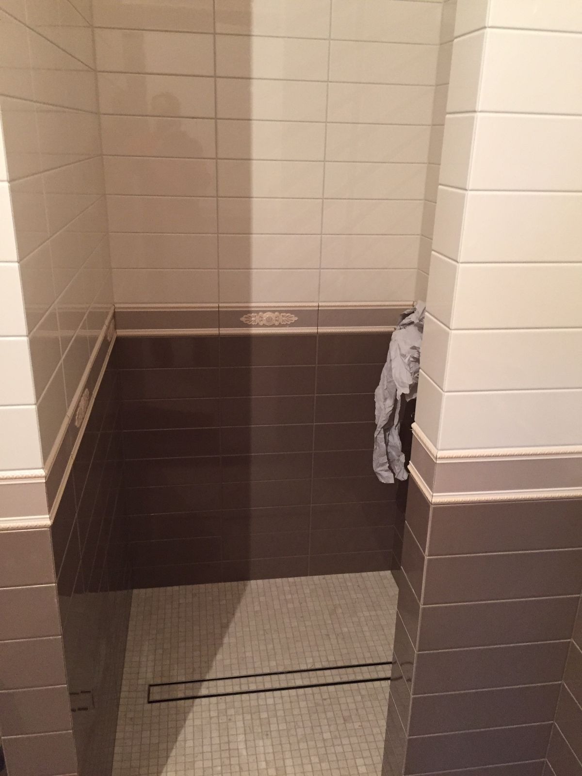 Wykończona kabina prysznicowa z brązowo-białymi płytkami, dekoracyjnym pasem i odpływem liniowym. Widok z góry, wnętrze łazienki po remoncie.