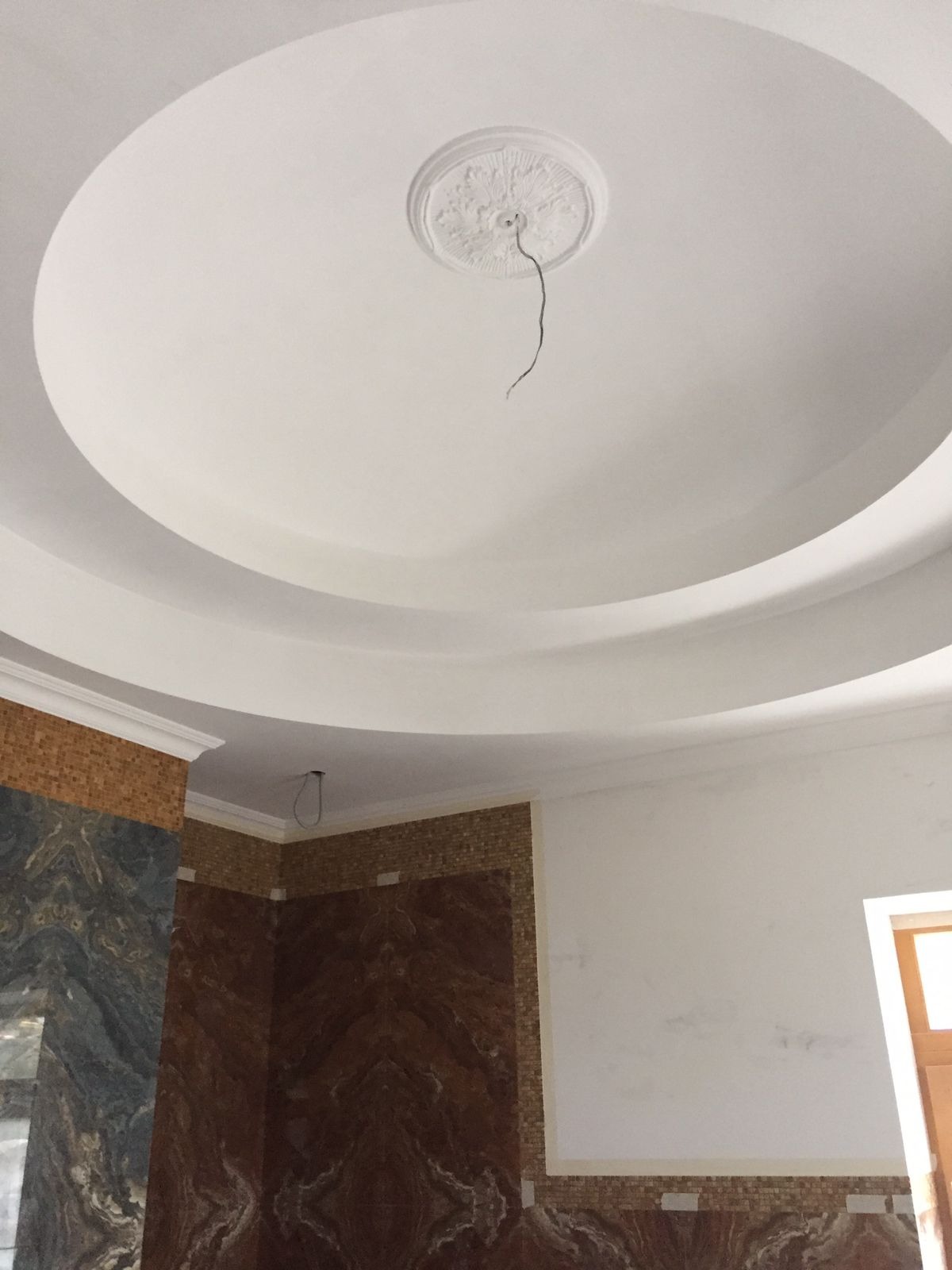 Biały, okrągły sufit podwieszany z dekoracyjnym elementem centralnym i wystającym przewodem. Fragment ściany wykończony mozaiką i płytami imitującymi marmur.