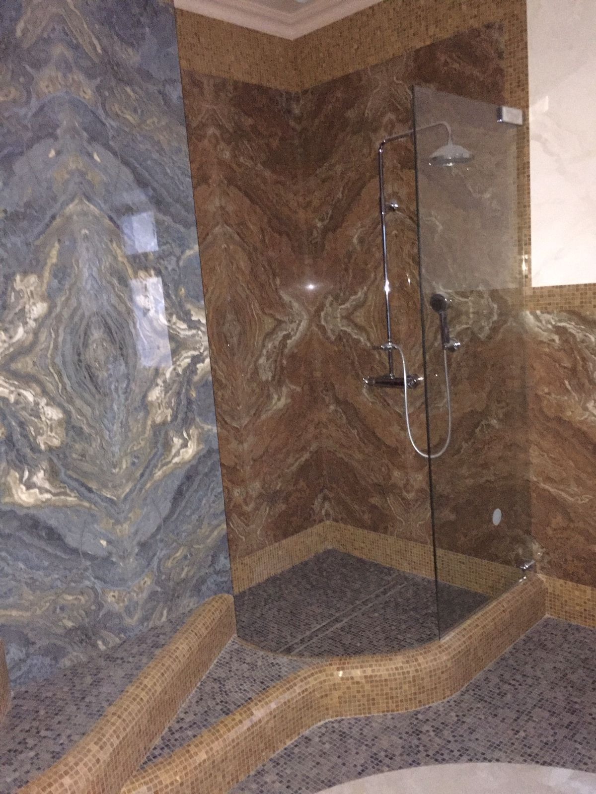 Luksusowa kabina prysznicowa z marmurowymi ścianami w odcieniach brązu i szarości, wykończona mozaiką. Nowoczesny design z elementami dekoracyjnymi.