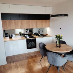 Przestrzeń z Pasją - Nowoczesna kuchnia z lustrzanym panelem nad blatem, drewnianymi szafkami i okrągłym stołem z szarymi krzesłami. Minimalistyczny design, ciepłe oświetlenie.