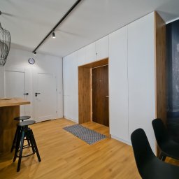Przestrzeń z Pasją - Nowoczesne wnętrze: białe szafy w zabudowie, drewniane akcenty, designerska lampa i podłoga. Minimalistyczny przedpokój z elementami dekoracyjnymi.