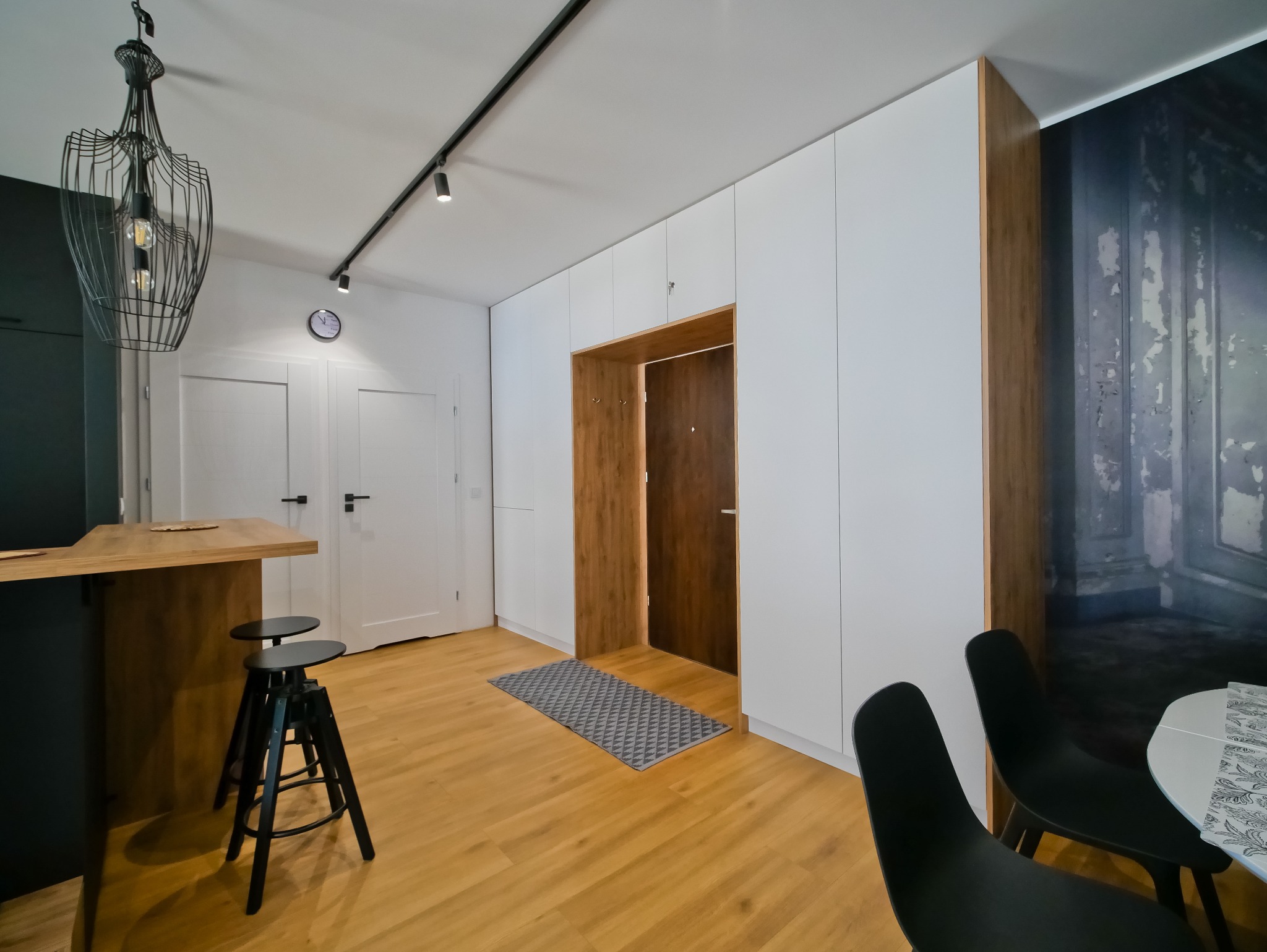 Nowoczesne wnętrze: białe szafy w zabudowie, drewniane akcenty, designerska lampa i podłoga. Minimalistyczny przedpokój z elementami dekoracyjnymi.