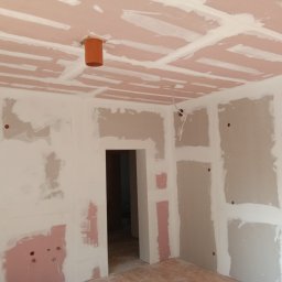 FachNaTak - Pokój w trakcie prac wykończeniowych: ściany i sufit pokryte płytami gipsowo-kartonowymi, widoczne łączenia i otwory instalacyjne. Pomieszczenie przygotowane do szpachlowania.