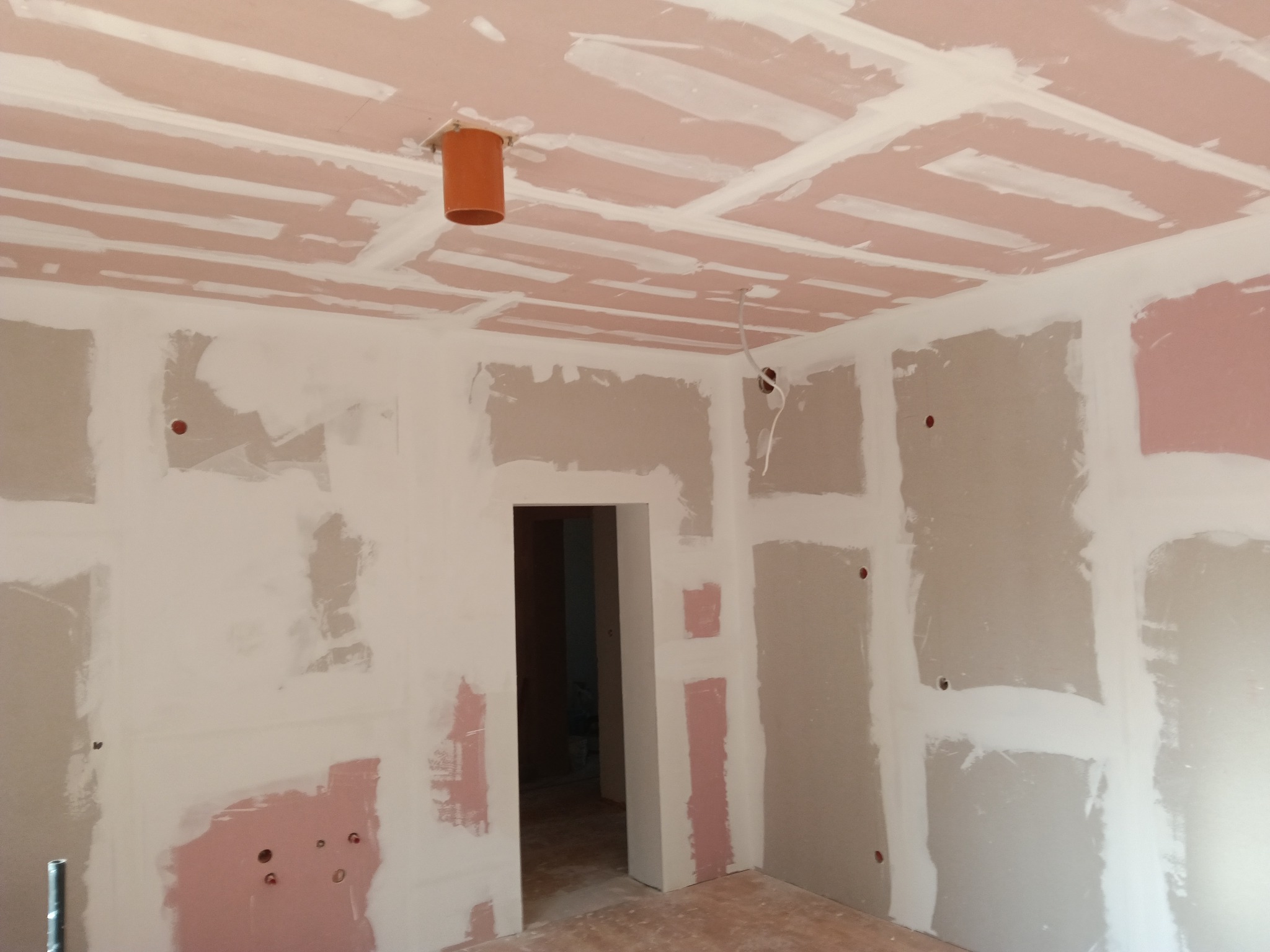 Pokój w trakcie prac wykończeniowych: ściany i sufit pokryte płytami gipsowo-kartonowymi, widoczne łączenia i otwory instalacyjne. Pomieszczenie przygotowane do szpachlowania.