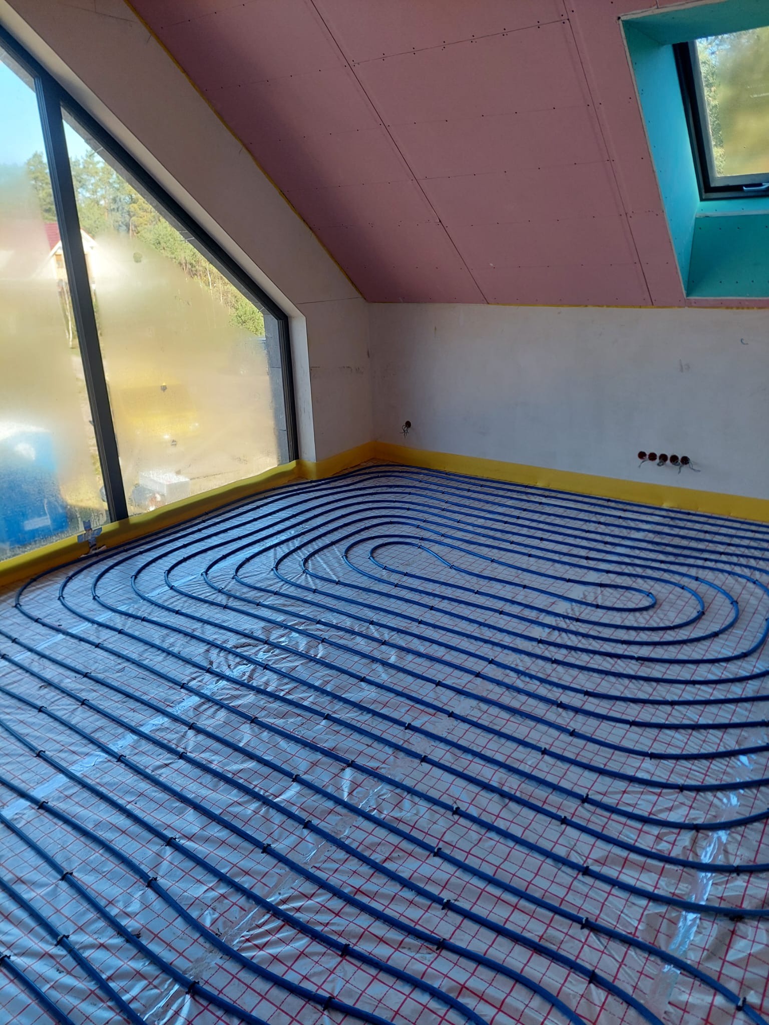 Instalacja ogrzewania podłogowego z rur w kształcie spirali, widok z góry, na podłodze folia izolacyjna, ściany przygotowane do dalszych prac wykończeniowych.