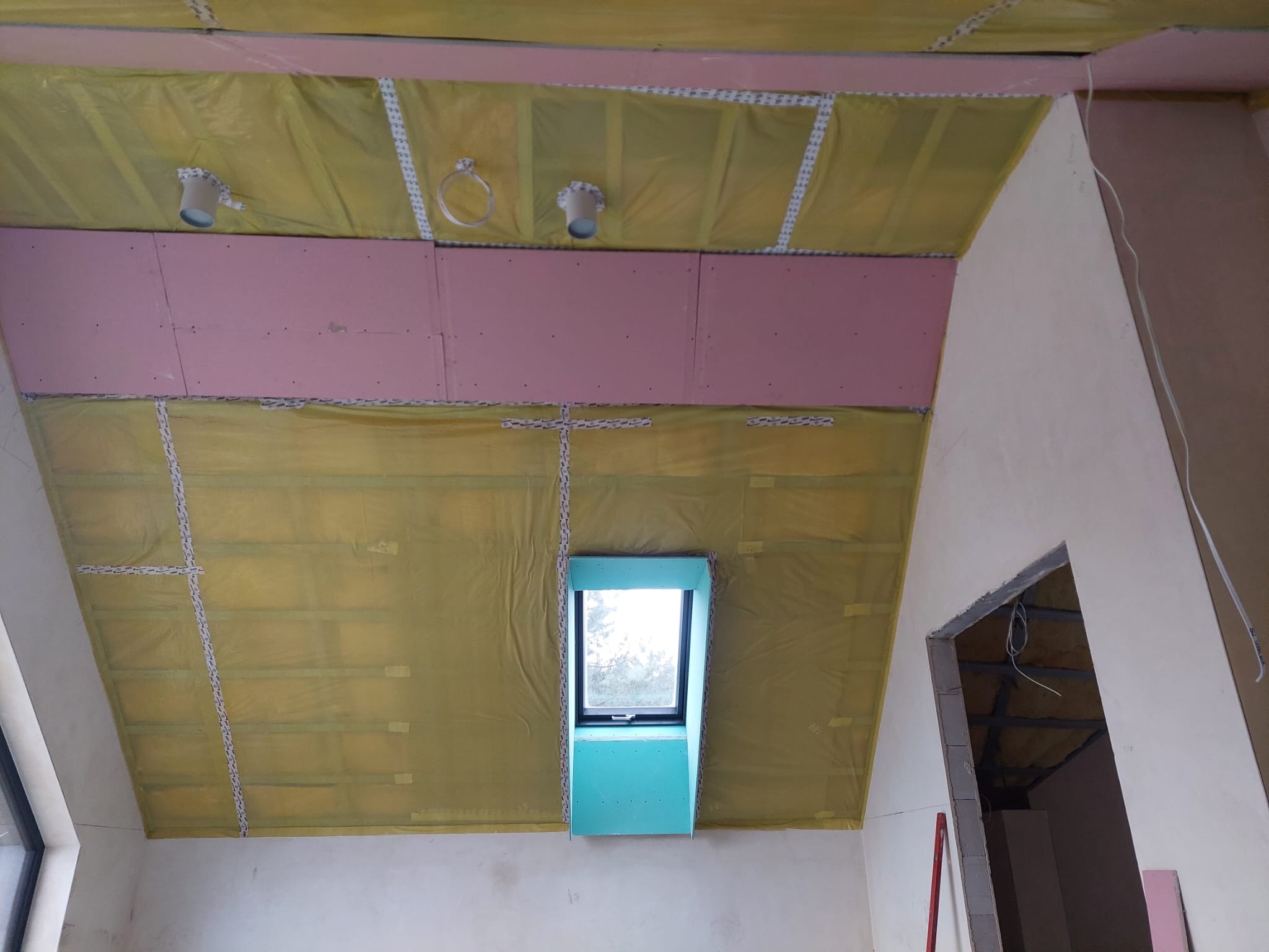 Poddasze w trakcie adaptacji w Szczecinie: izolacja folią, płyty karton-gips na skosach, okno dachowe w obudowie z płyty. Widoczne przygotowania do wykończenia.