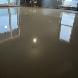 RevoArt - Błyszcząca, gładka, szara posadzka żywiczna w nowym wnętrzu. Widoczne odbicie okien i światła. Ściany zabezpieczone folią malarską.