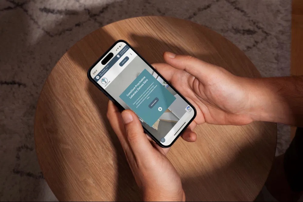 Osoba trzyma smartfon z otwartą stroną internetową Consilium Przychodnia Lekarska Zielona Góra na drewnianym stoliku, widok z góry.
