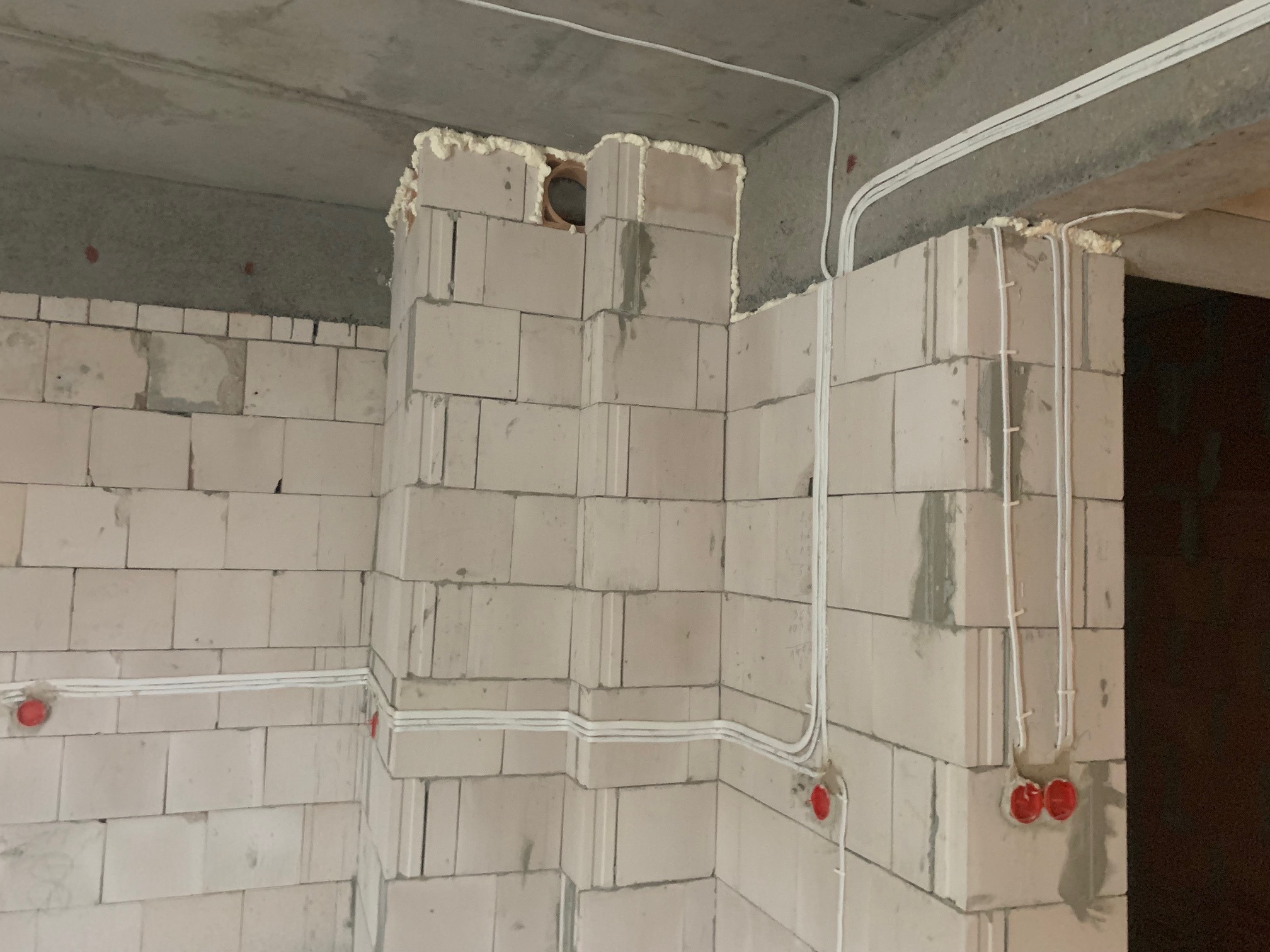Wewnętrzne kable elektryczne prowadzone po ścianie z pustaków, zabezpieczone pianką montażową w narożnikach. Widoczne czerwone puszki instalacyjne.