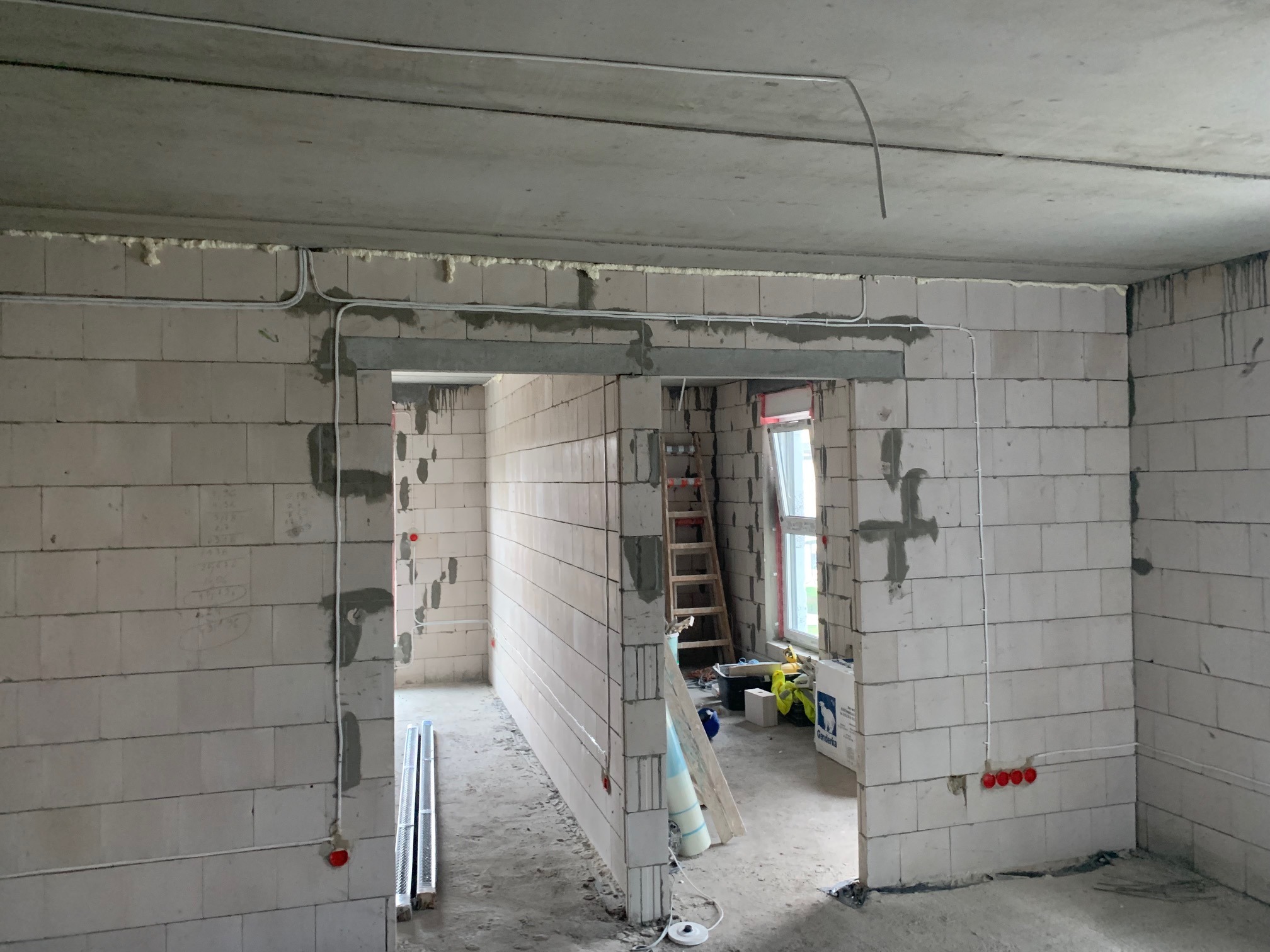 Wnętrze w trakcie prac: białe kable elektryczne prowadzone po ścianach z betonu komórkowego, widoczne puszki instalacyjne. Surowy stan wykończenia.