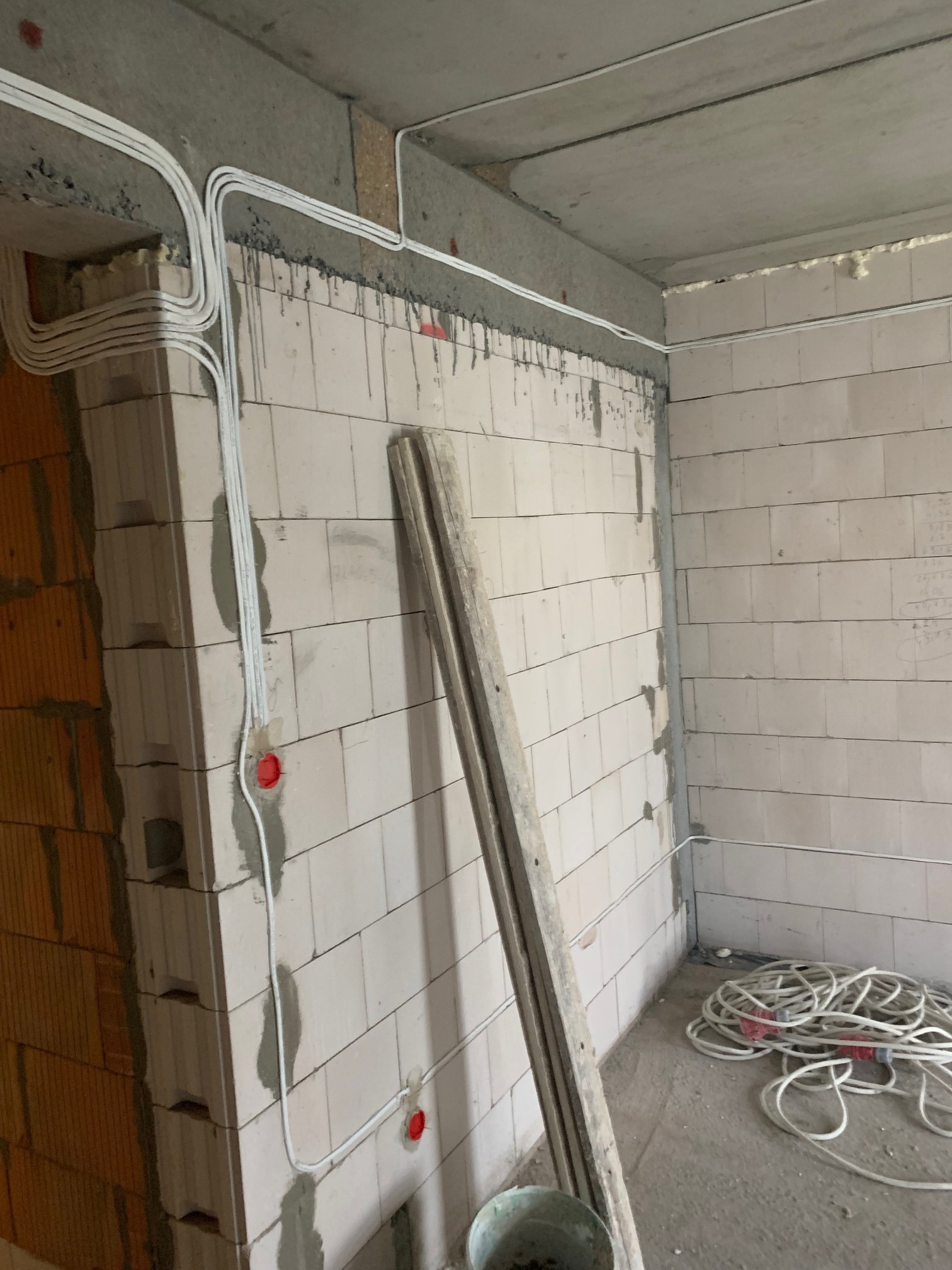 Wnętrze w trakcie prac elektrycznych: białe kable prowadzone po ścianach z betonu komórkowego, widoczne puszki instalacyjne i zwój kabli na podłodze. Surowy stan wykończenia.